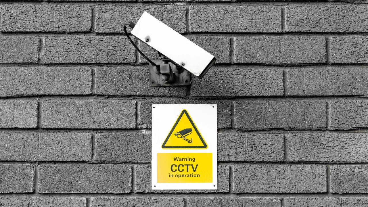A CCTV camera with a warning sign beneath it
